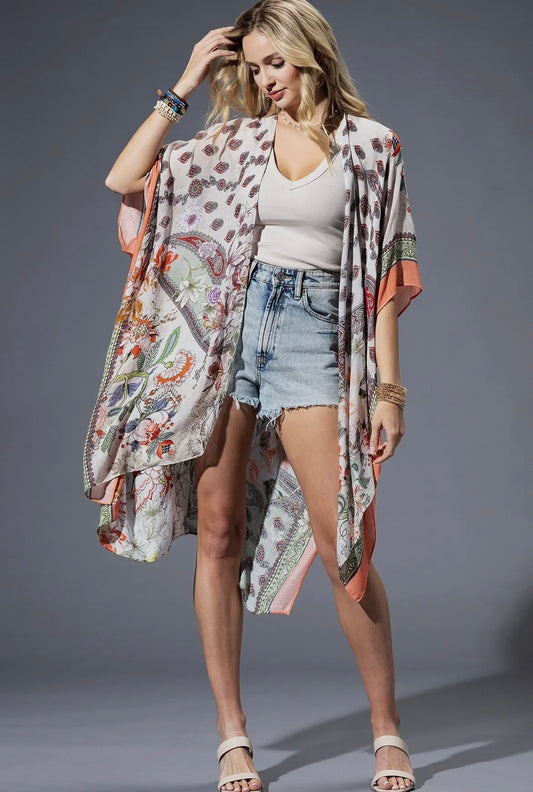 Woman wearing the Sienna Kimono with soft orange and green floral print, styled with denim shorts and white tank.