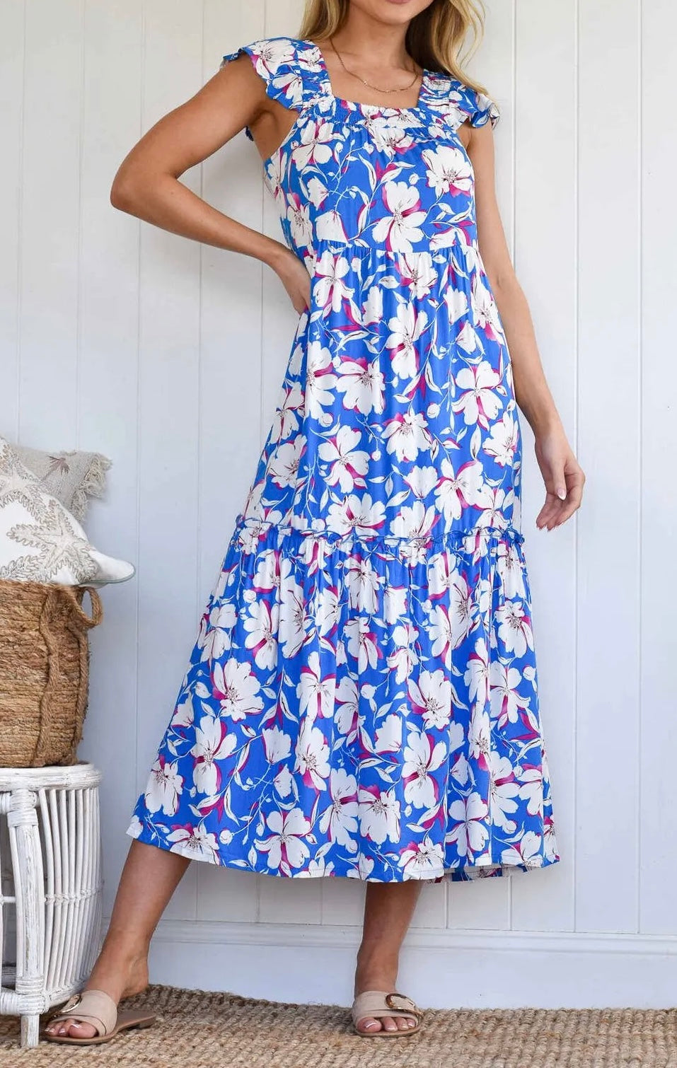 A close up on a woman wearing a blue midi dress with a white and pink floral pattern, cap sleeves, and an open-back design.