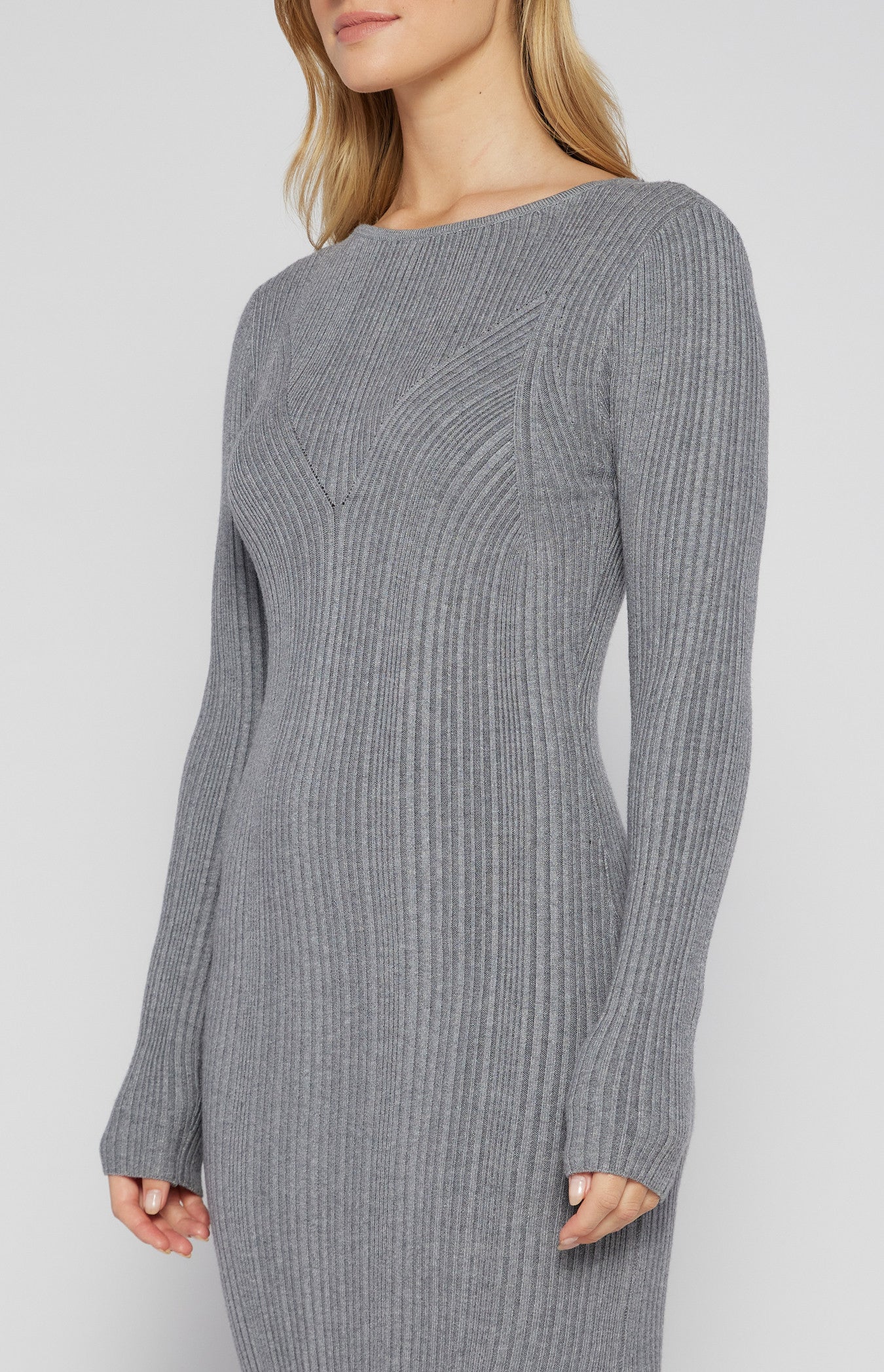 Woman wearing a long sleeve grey ribbed knit bodycon midi dress with a side slit and scoop neckline, styled with black heels torso shot