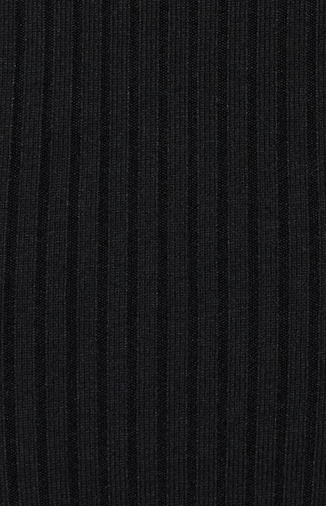 Woman wearing a bodycon black one-shoulder ribbed knit midi dress with long sleeves and side slit, styled with nude heels rib close up