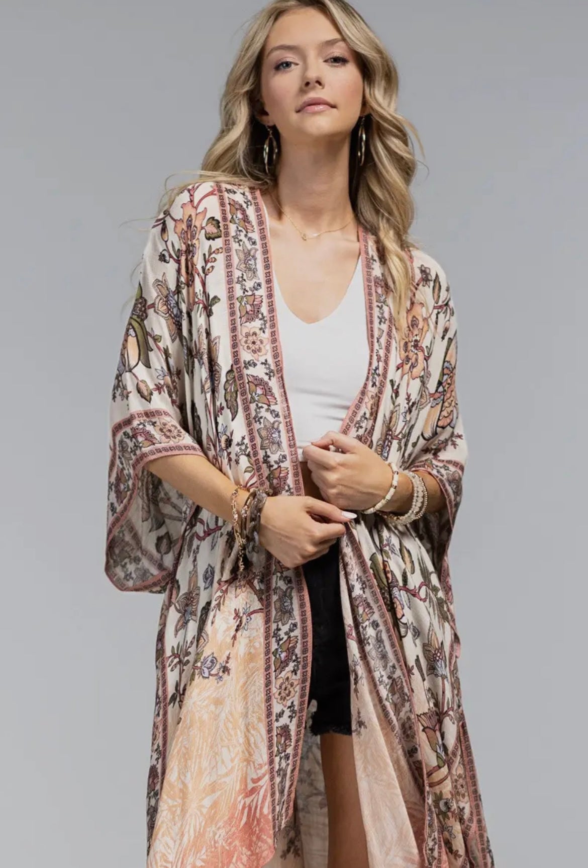 Woman wearing a boho floral kimono with wide sleeves and open front, layered over a white tank and black shorts high shot