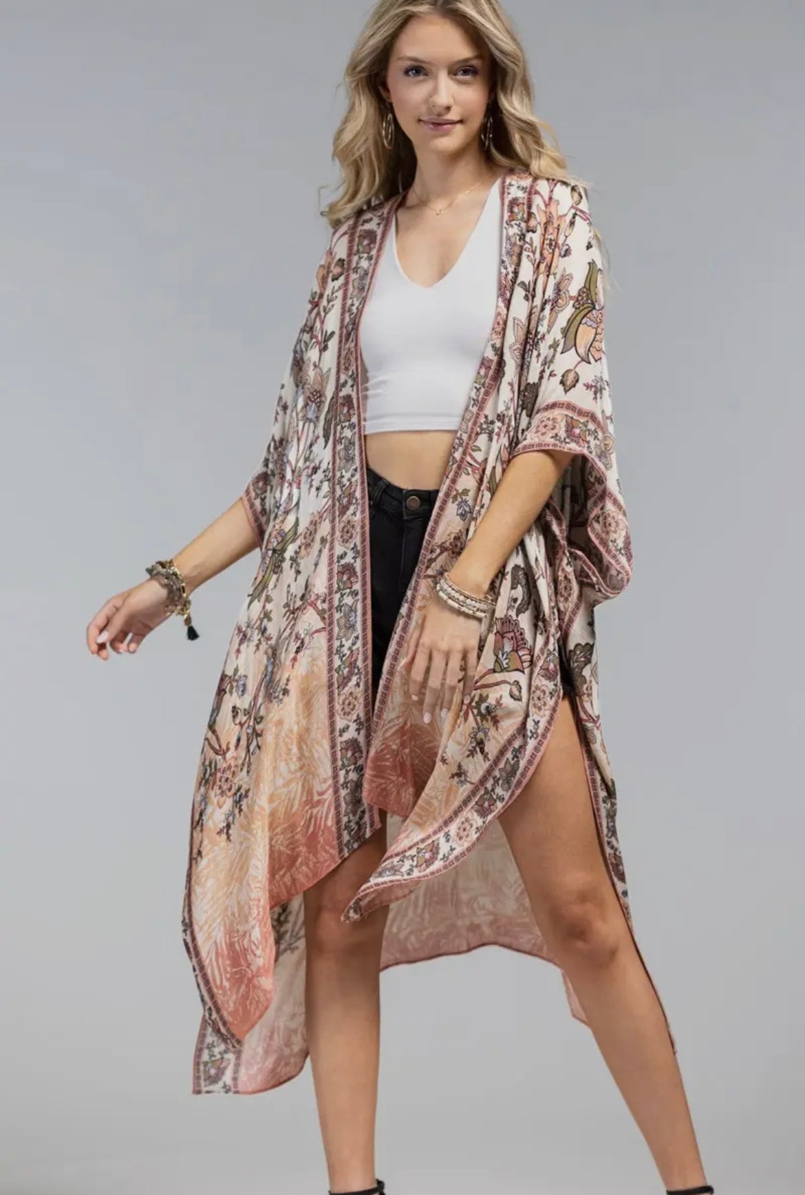 Woman wearing a boho floral kimono with wide sleeves and open front, layered over a white tank and black shorts full body