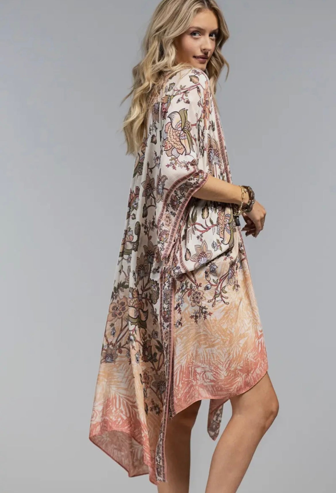 Woman wearing a boho floral kimono with wide sleeves and open front, layered over a white tank and black shorts side shot