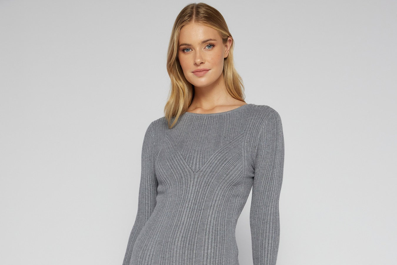 Woman wearing a long sleeve grey ribbed knit bodycon midi dress with a side slit and scoop neckline, styled with black heels